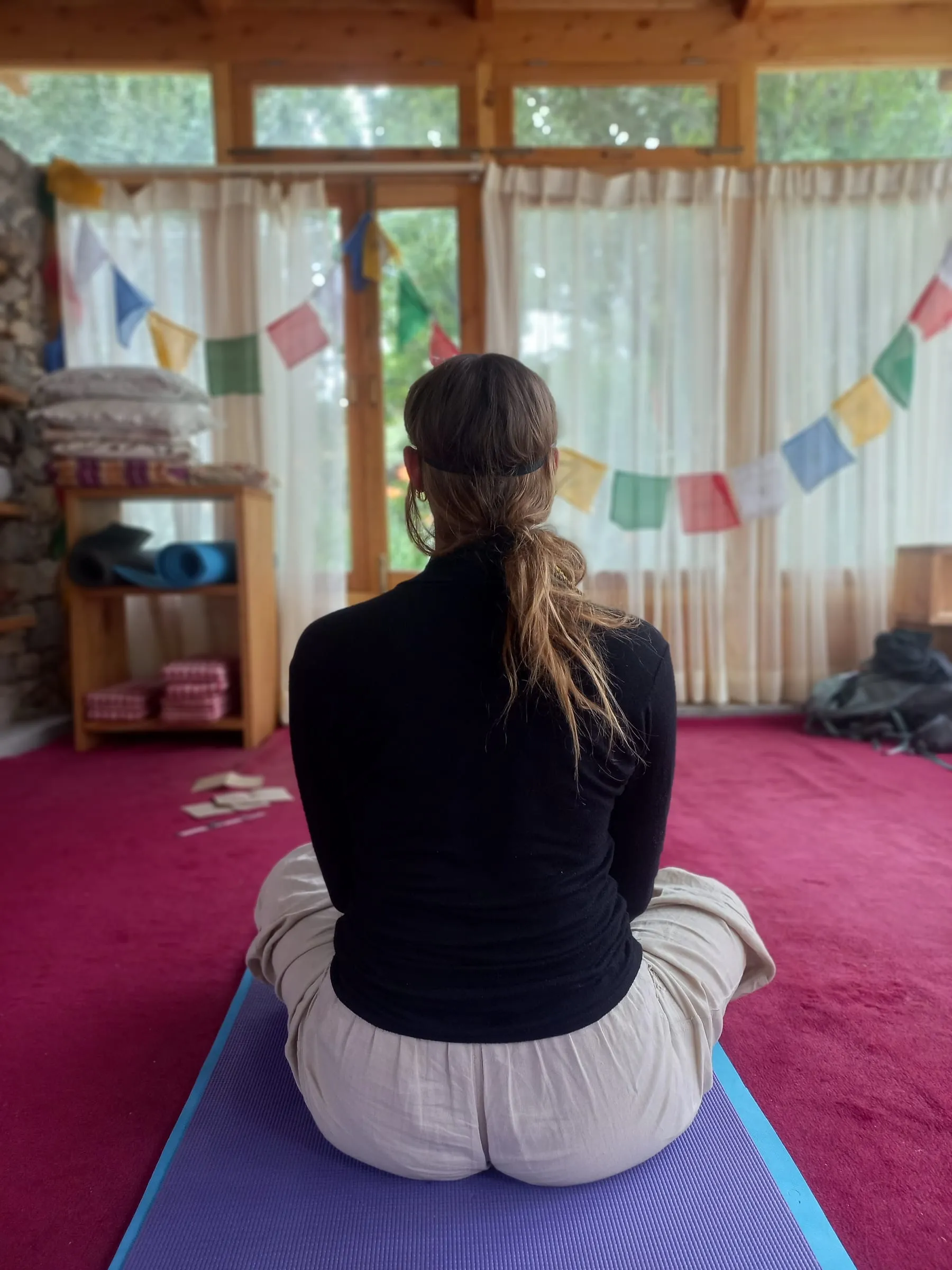 Someone sitting on their mat, seen from behind, facing prayer flags