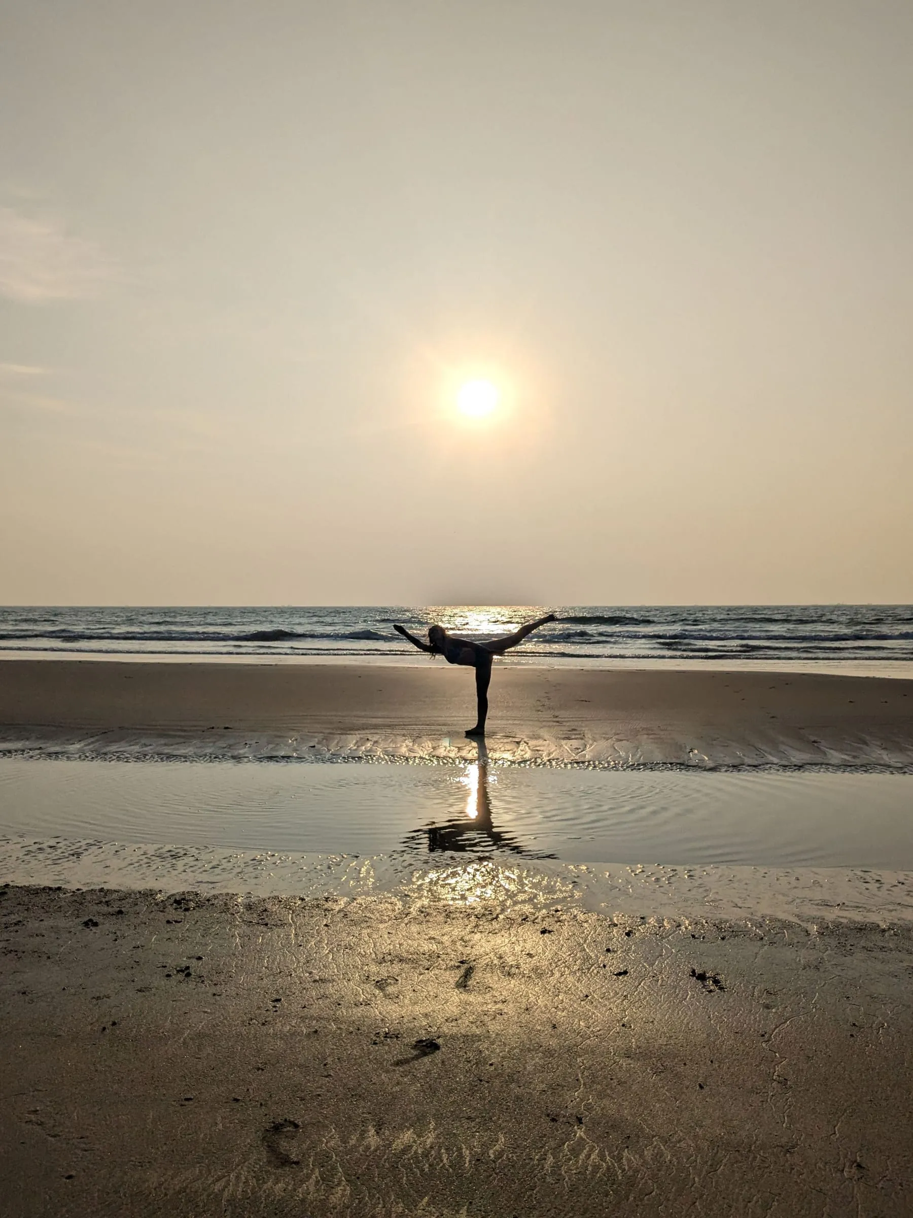 Laura in a standing balance on a beach, the sun low over the sea