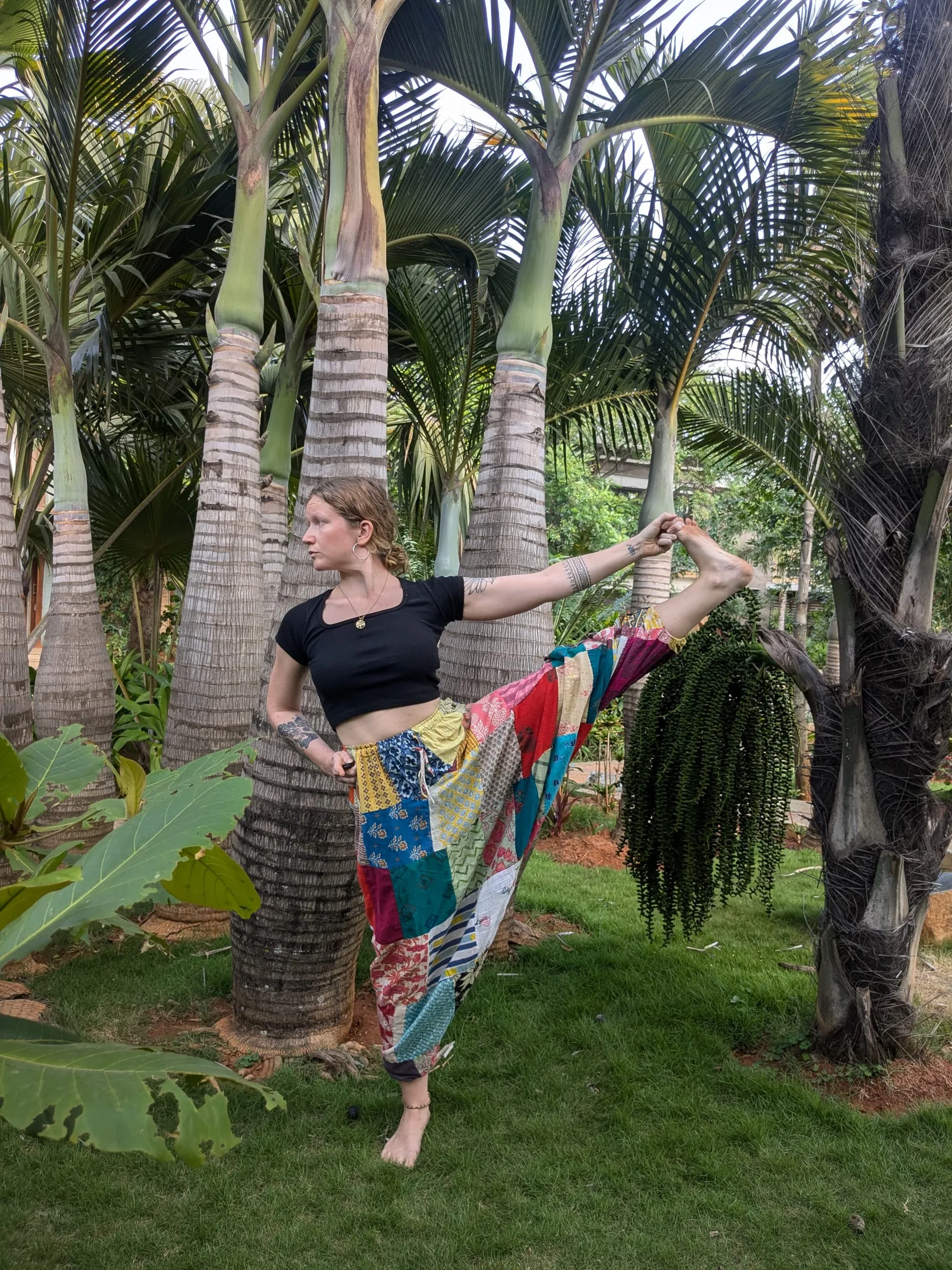 Laura balancing on one leg in a palm garden, holding the big toe of her raised leg out to the side