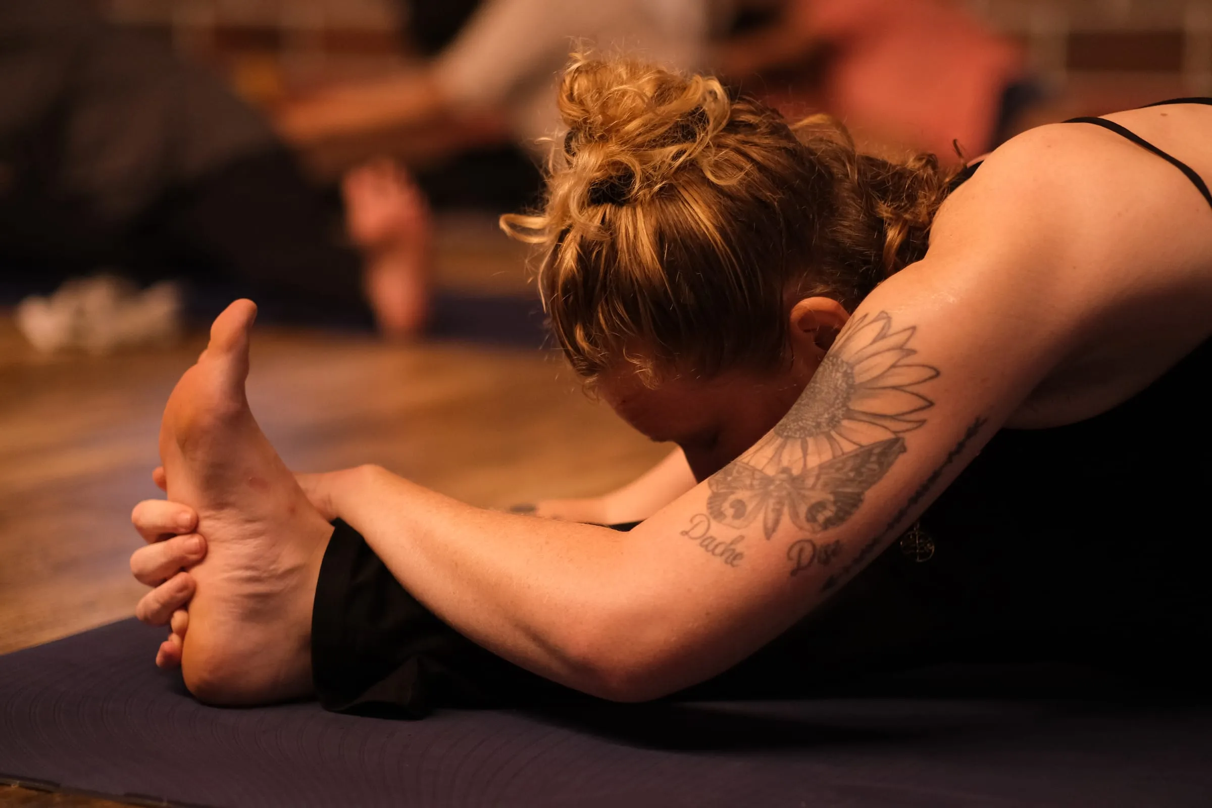 Laura folding forward over her outstretched leg, holding her foot, in a warmly lit studio