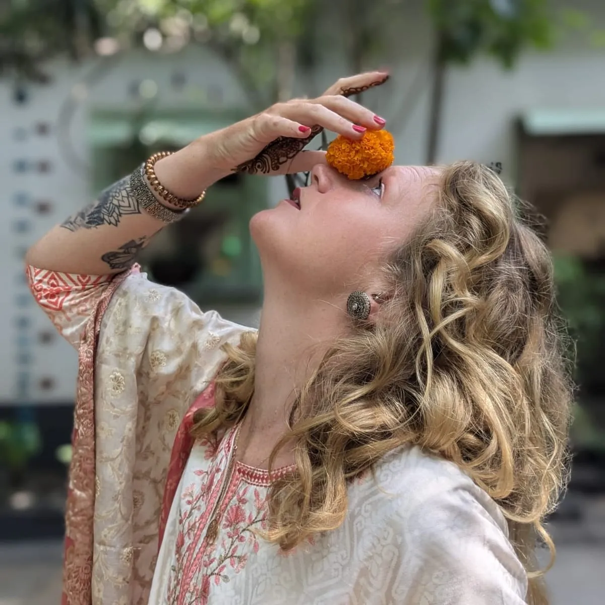 Laura in a cream and coral kurta, holding a marigold flower to her face