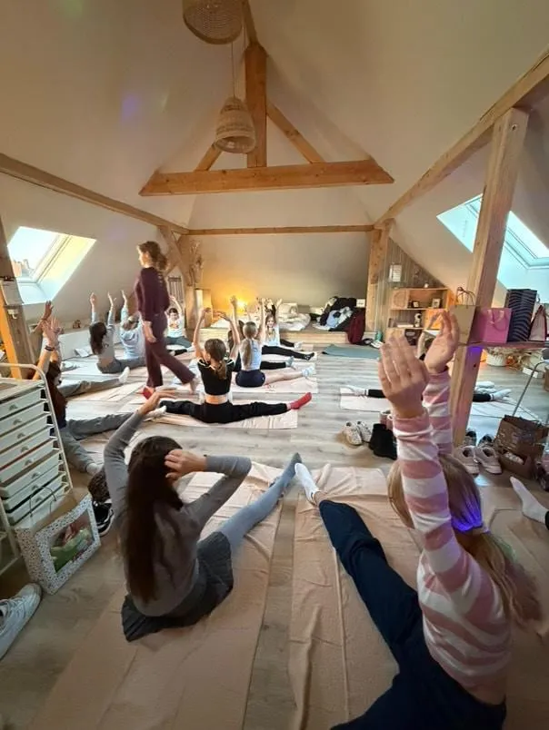 A group practising yoga together in a wooden attic room, Laura walking between the mats