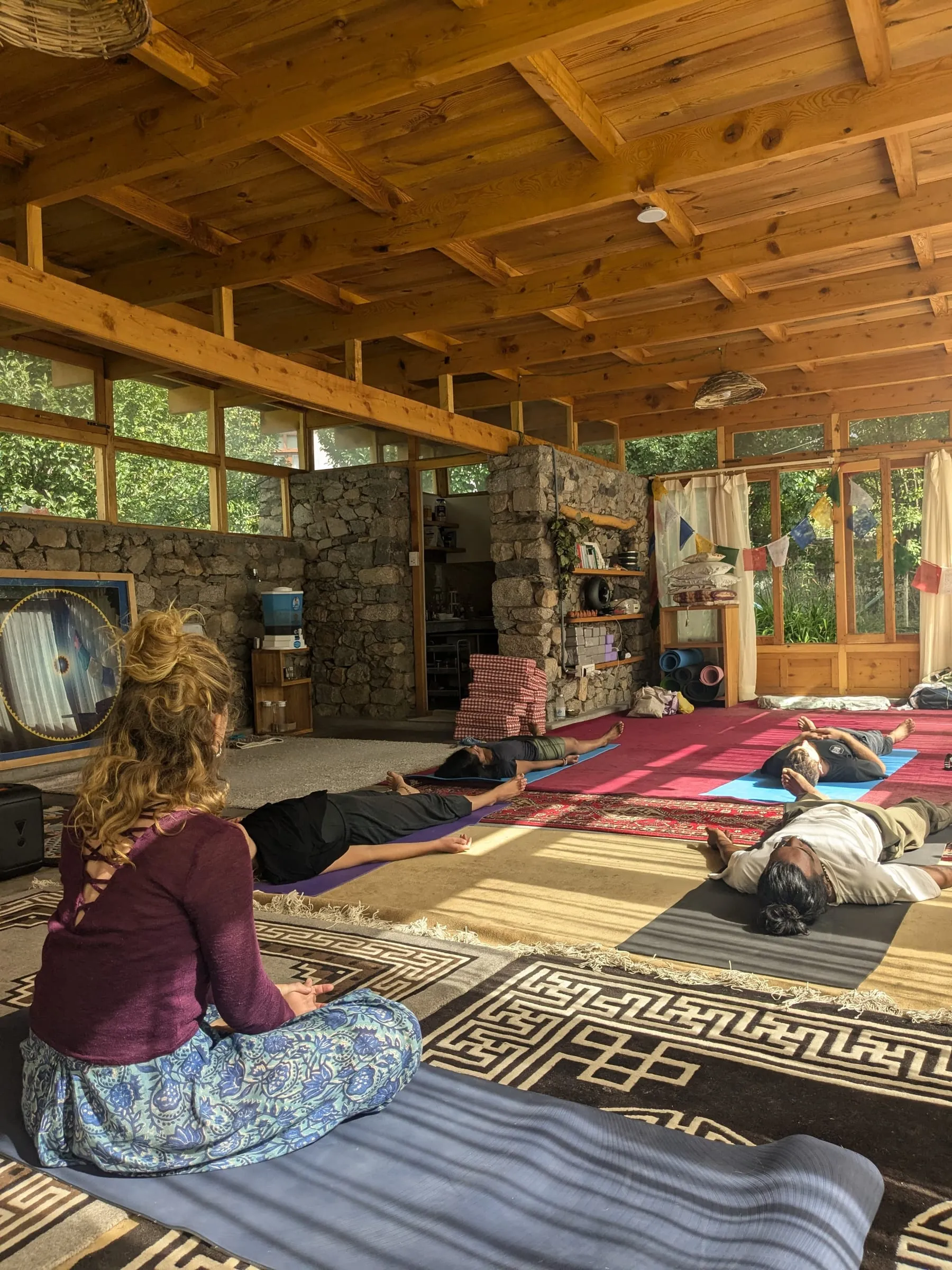 Laura sitting before a group resting on their mats in a wooden studio