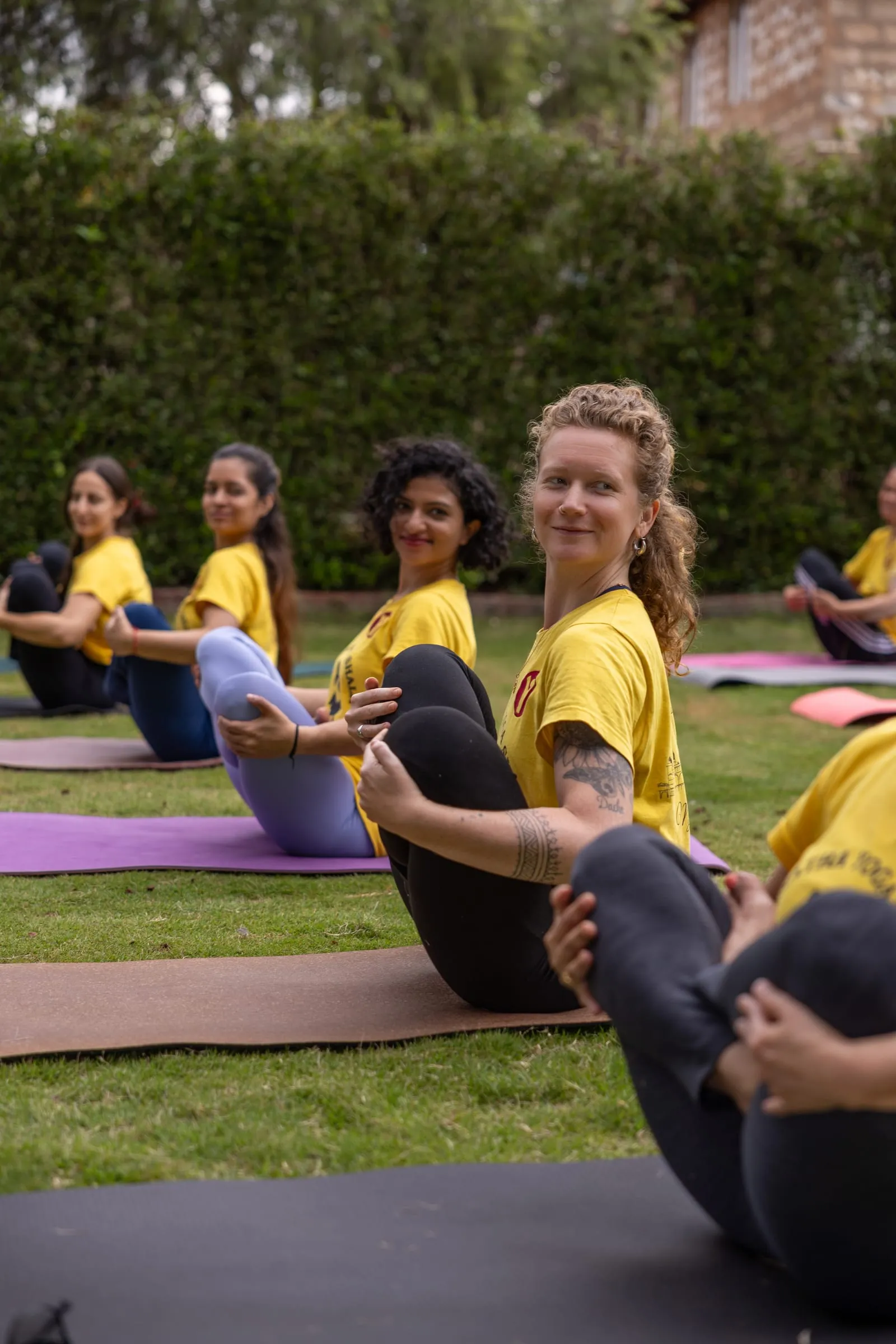 Laura smiling among a group of practitioners seated on mats on a lawn